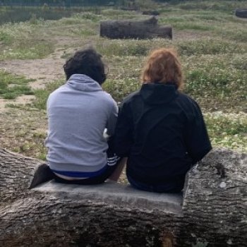 The backs of two people sitting on a stone plnth