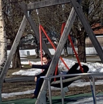 Two adults on a large swing with snow and tress in the background